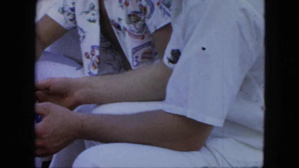 Tight home-movie frame of seated adults in white clothing, cropped at the arms and torso, with the blue ball partly visible near the edge.