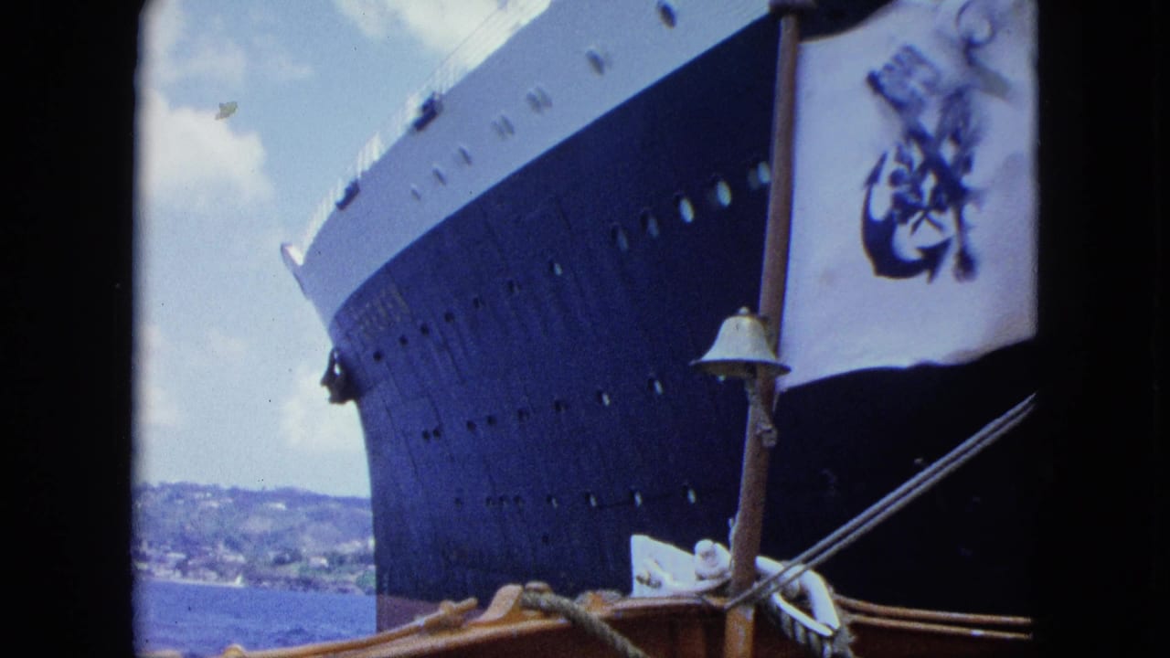1964 8mm frame showing a close pass by a dark ocean liner hull, small boat rigging, and a white flag with a blue pirate-style emblem.