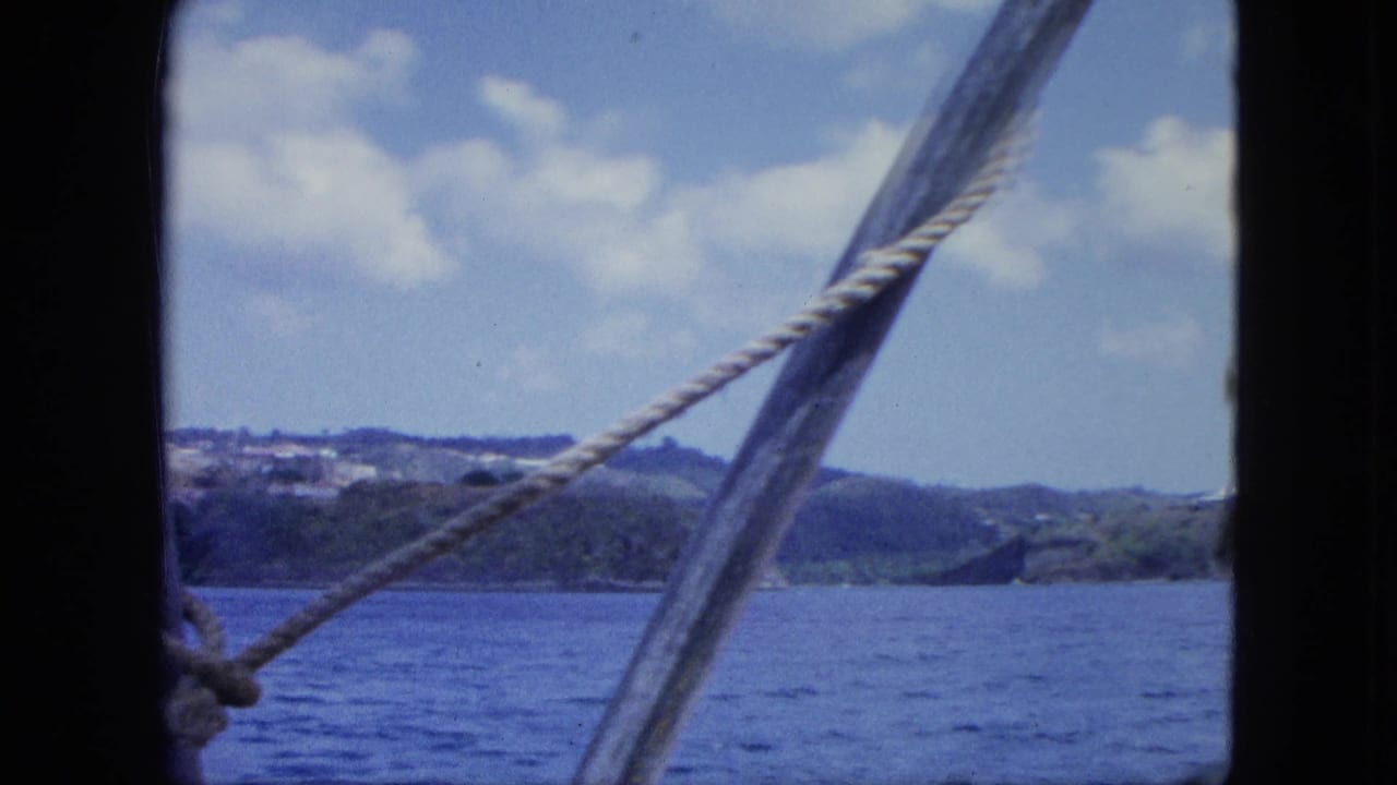 Boat-side view of blue water and green hills, with diagonal rope and dark framing visible in this 1964 home-movie frame.