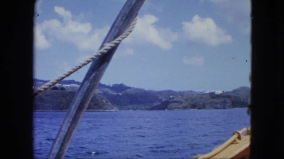 1964 boat view across open water toward green hills, with rigging and a small section of deck in the foreground.