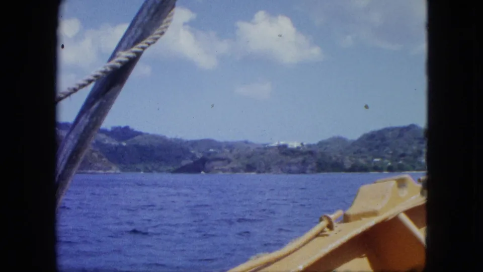 Final 1964 home-movie frame shows blue sea, hilly coast, boat rope, and a yellow deck section from a passenger viewpoint.