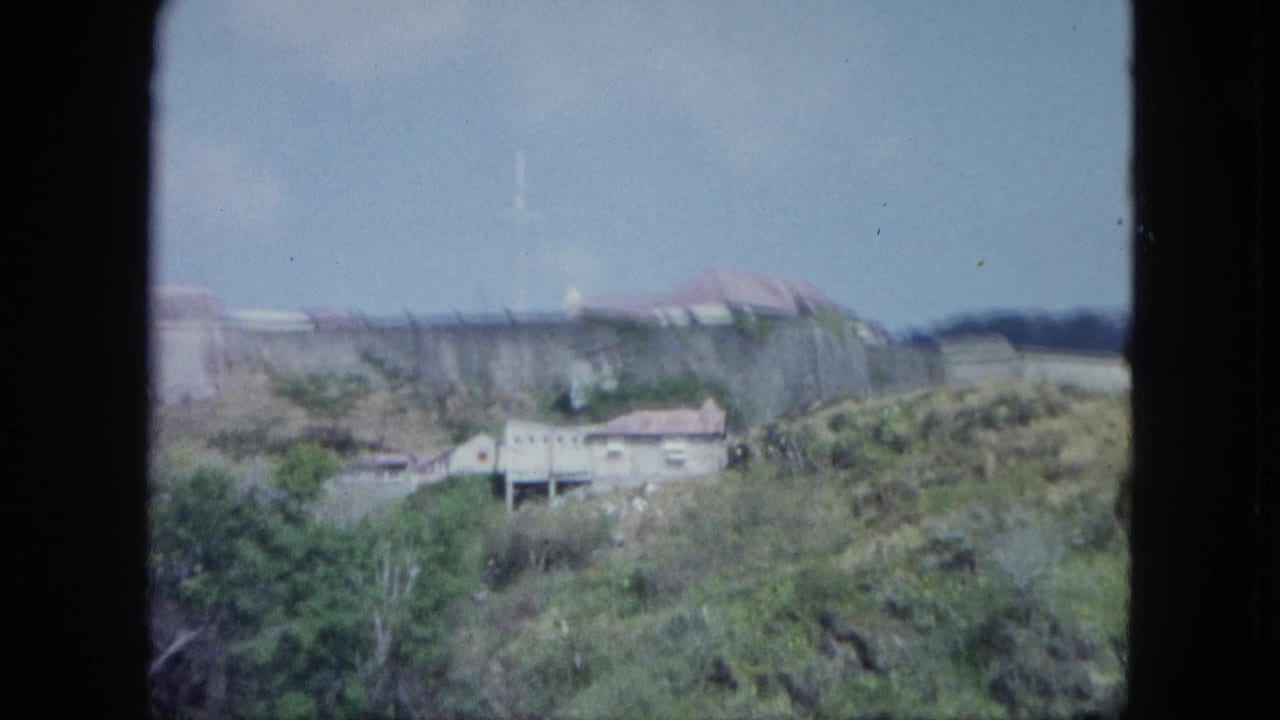 Cataloged Martinique 8mm frame of a walled hillside site with small light buildings and dense tropical vegetation.