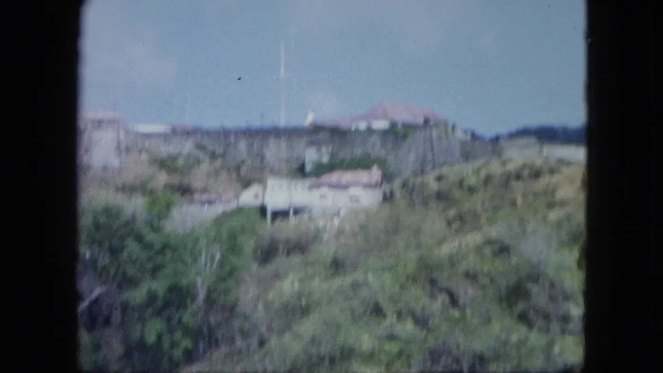 Soft 8mm view of the hillside walls and buildings, with brush and tropical growth filling the foreground.