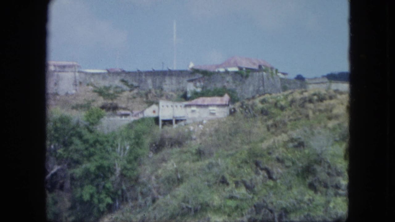 Soft 8mm view of pale buildings and walls set among rocky vegetation on a coastal hillside, with sky above.