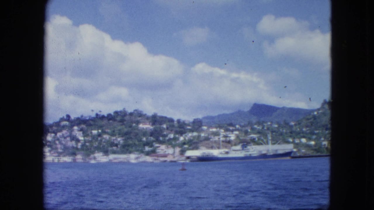 Coastal town on green hills beside blue water, seen through dark window edges.