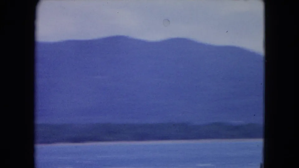 A soft 8mm view of blue water, low shoreline, and hazy mountains near Montego Bay after the boat leaves the frame.