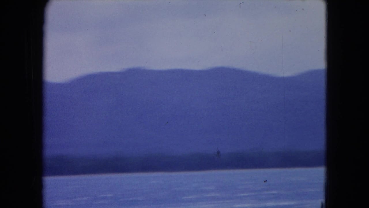Blue sea below hazy mountains and pale sky, framed by 8mm film borders.