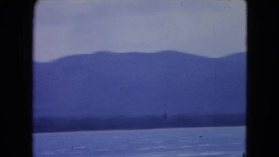 1964 Montego Bay 8mm frame showing blue water, distant hazy mountains, and pale sky with visible film-gate edges.