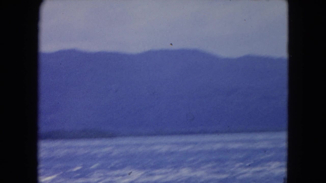 Open blue water with distant mountain ridge under a pale sky.