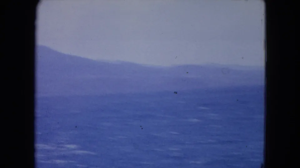 1964 Jamaica coastal view with rippled blue water, low haze, and layered hills receding across the horizon.