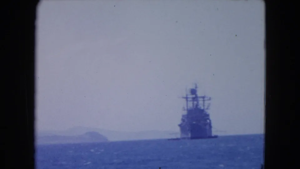 1964 Montego Bay frame showing a large ship near the horizon, with low landforms behind it and blue water in the foreground.