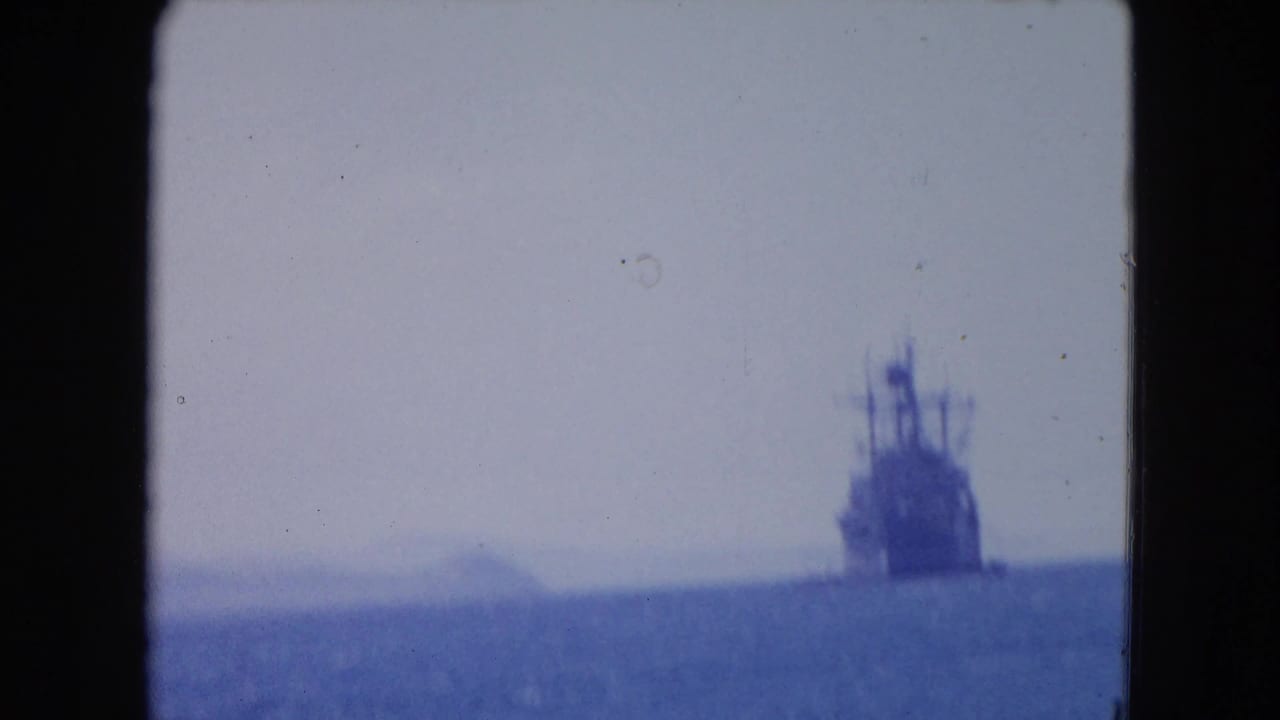 Distant naval ship silhouette on the horizon under a hazy sky.