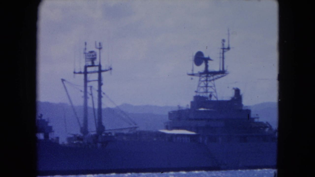 1964 Montego Bay home-movie frame showing a large ship with radar and mast structures in a harbor, with mountains in the distance.