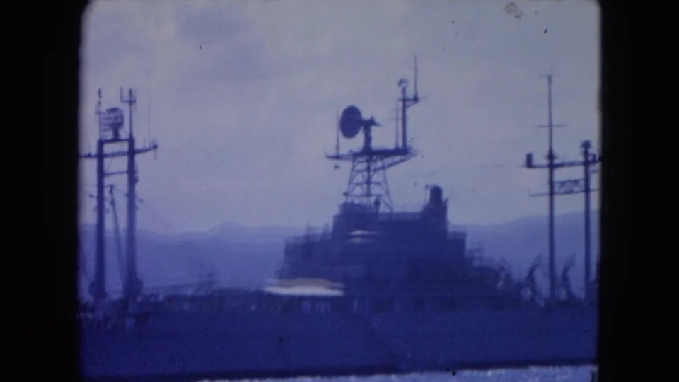 A distant radar-equipped vessel in Montego Bay harbor, filmed in 1964 with blue-tinted 8mm color and mountains behind it.