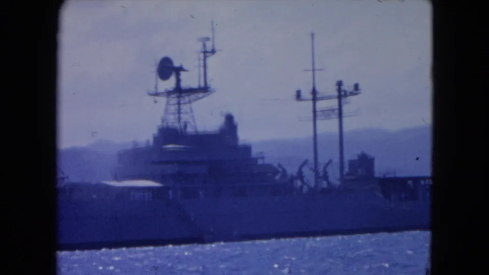 Montego Bay harbor frame from 1964 showing the vessel’s radar dish, masts, and upper deck against a hazy mountain backdrop.