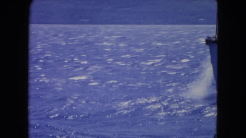 1964 Montego Bay 8mm frame showing shimmering open water, a foamy wake at the right edge, and distant hills under a blue cast.