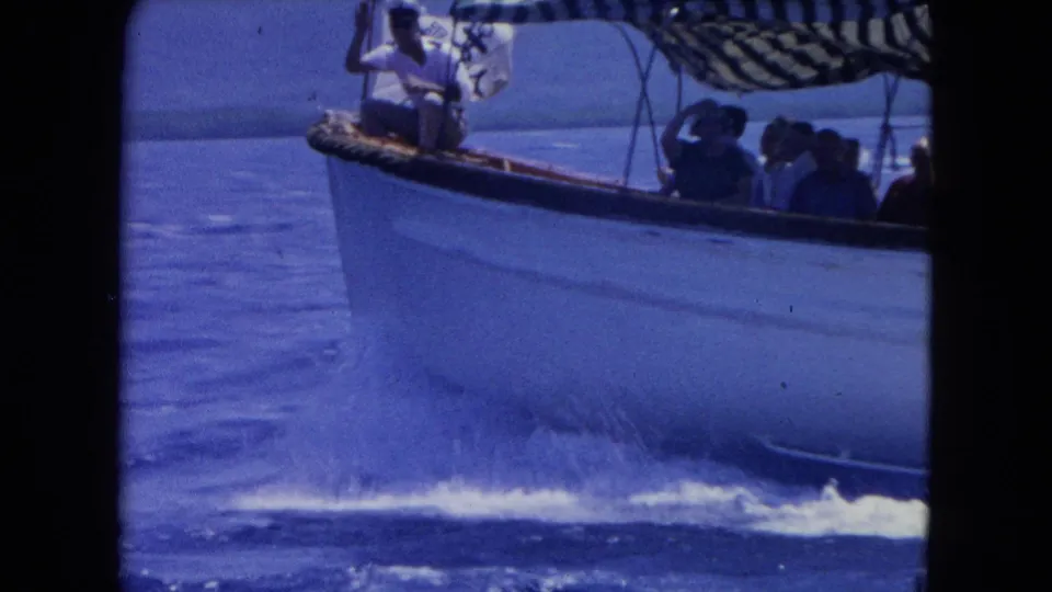 1964 Montego Bay 8mm side view of a white excursion boat with passengers seated under a striped canopy.