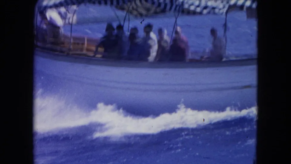 1964 Montego Bay 8mm frame showing a moving passenger boat, striped canopy, and foamy wake in blue water.
