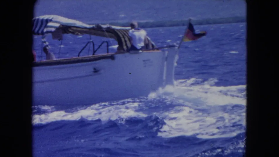 Small boat near Montego Bay with passengers under a striped canopy, a stern flag, and white wake on the sea.
