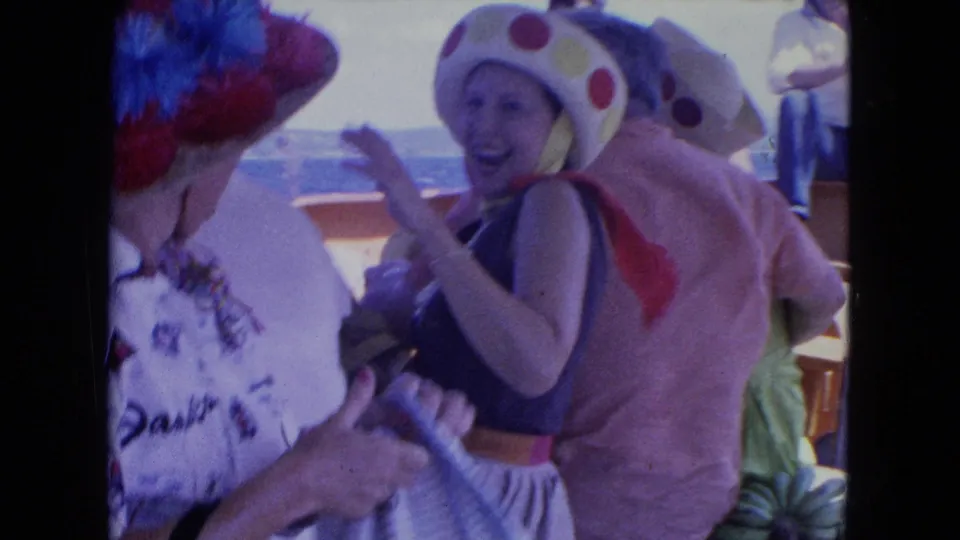 1964 Montego Bay home-movie frame showing a laughing woman in a polka-dot hat beside other adults on a boat deck.