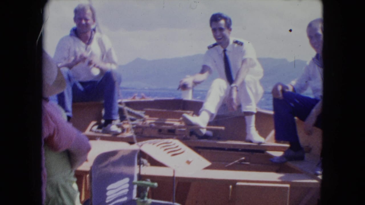 In 1964 Montego Bay home-movie footage, three men sit on a rocking wooden boat with sea and hills behind them.