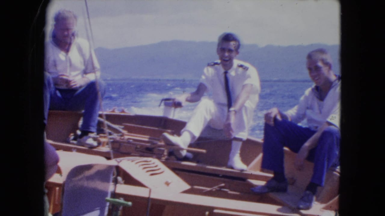 A uniformed man sits smiling on a boat with two other men nearby.