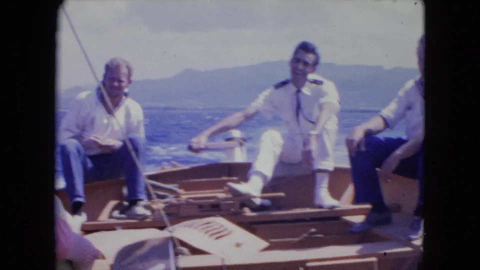 The uniformed man stretches an arm across the boat as other men sit nearby, with Montego Bay water and hills behind.