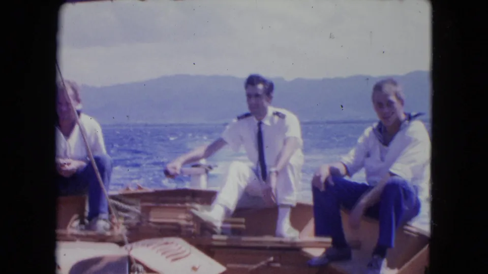 Montego Bay 8mm frame showing a uniformed man and casually dressed man seated on a boat, with another figure partly at left.