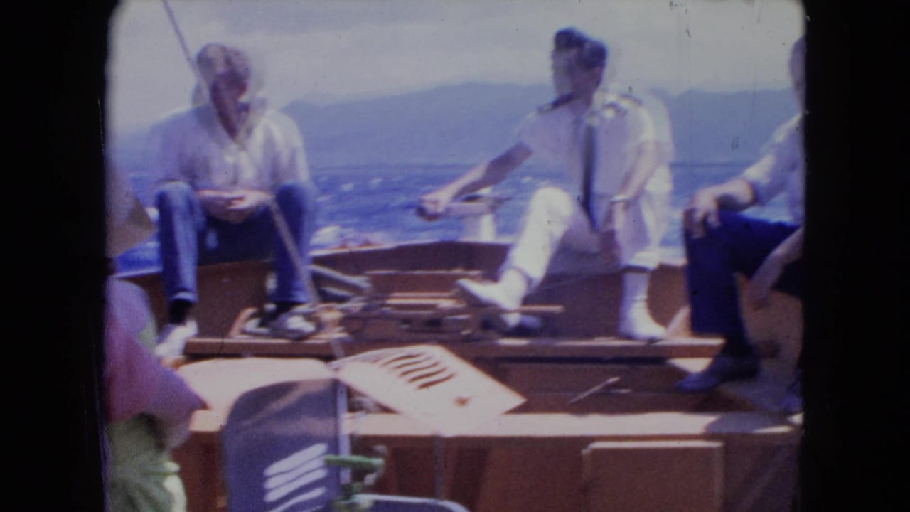 Adults seated on a wooden boat with ocean and distant shoreline behind them.