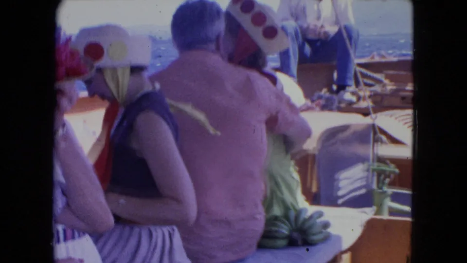 1964 Montego Bay vacation footage shows adults in novelty hats and warm-weather clothing seated together on a boat at sea.