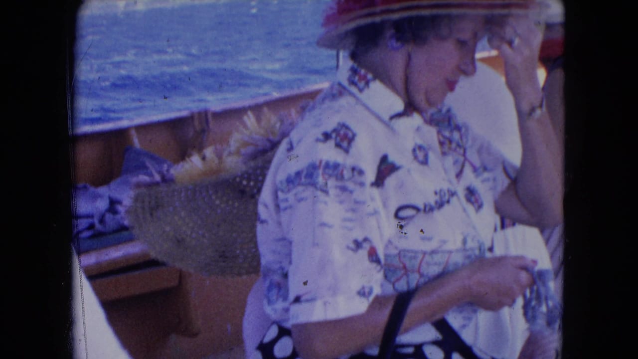 In supported 1964 Montego Bay footage, a woman in a feathered hat and patterned shirt adjusts her brim aboard a wooden boat.