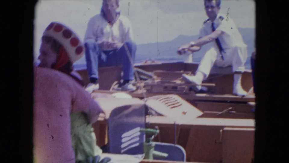 Passengers relax on a wooden boat deck during the 1964 Montego Bay outing, with coastal hills visible beyond the water.