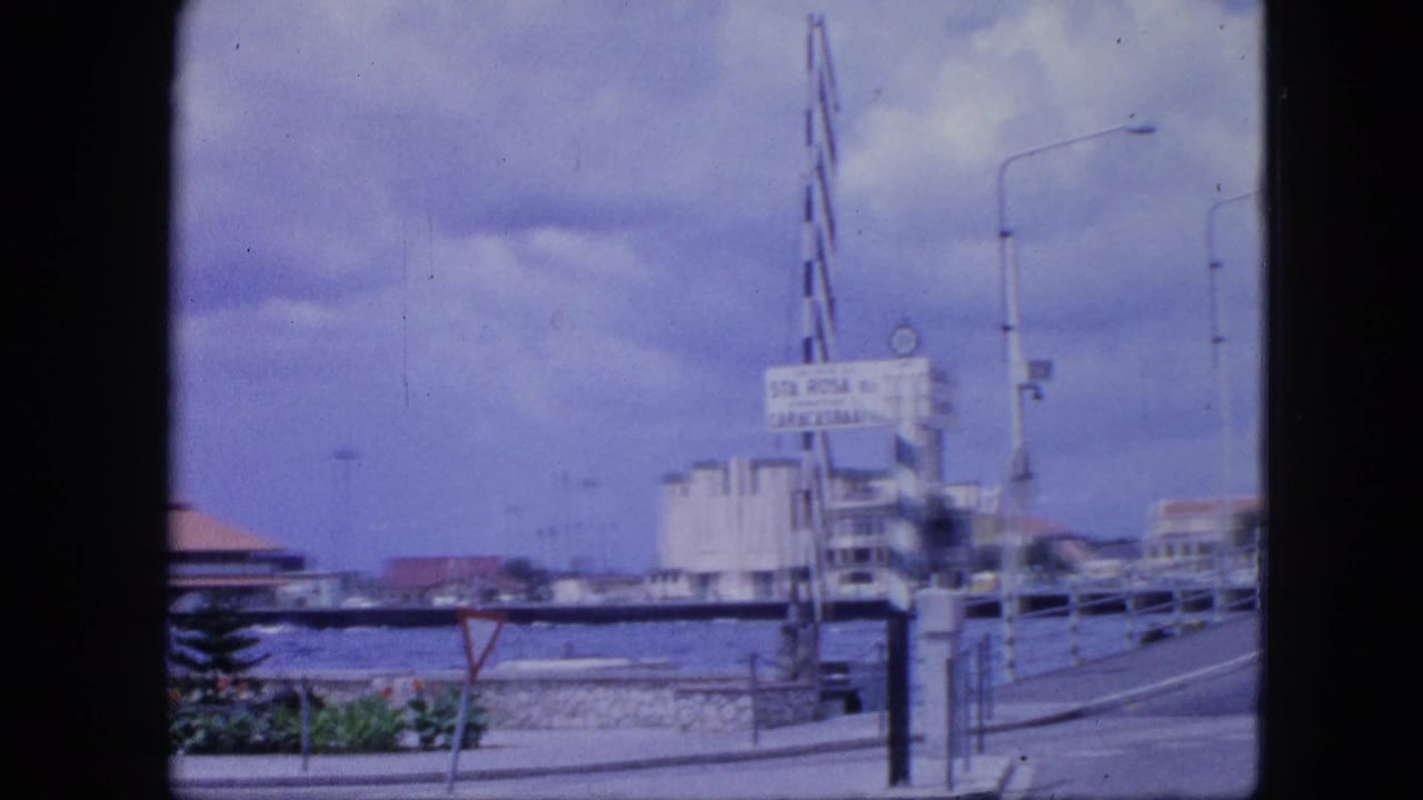 Harbor bridge entrance with a sign, striped pole, water, street lamps, and cloudy sky.