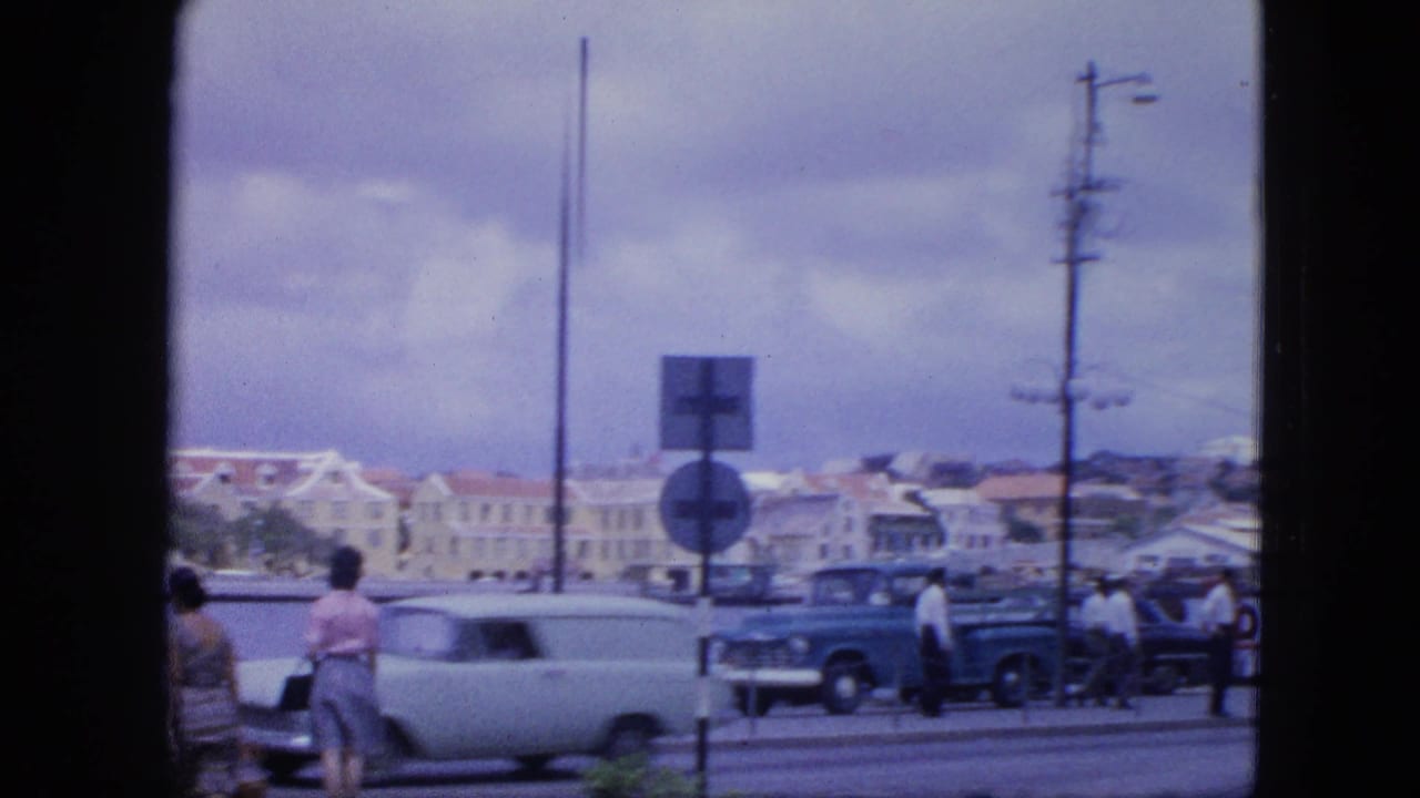 A light-colored car passes pedestrians beside the harbor road.