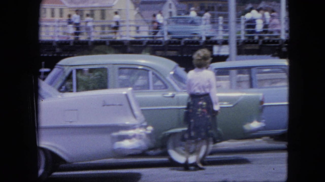 A woman stands near a green and white station wagon on a busy street.