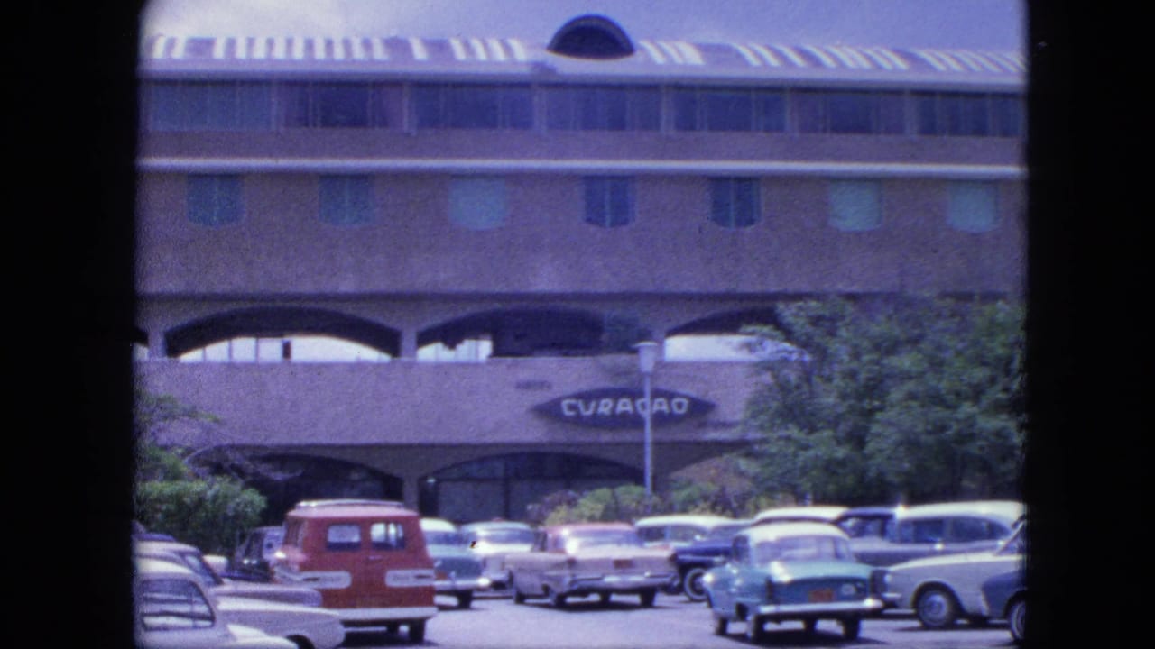 Classic cars parked before an arched building with the Curacao sign visible near center.