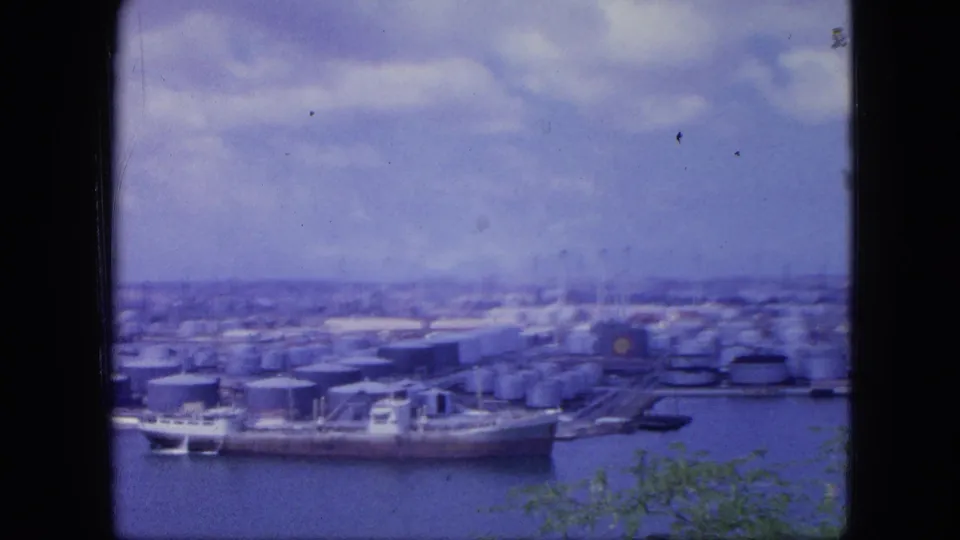 Wide 1964 Nassau port scene with tanker ships moored near cylindrical storage tanks and low industrial structures.