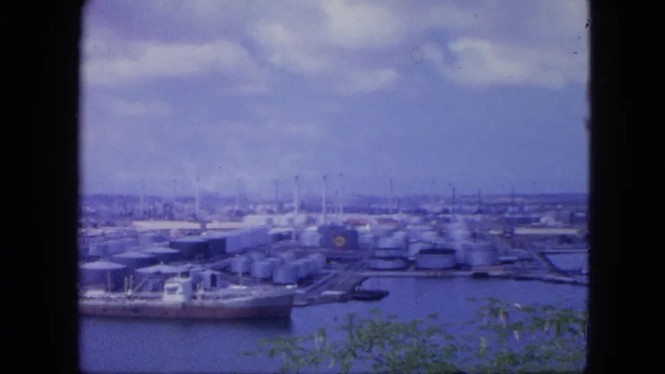 Nassau industrial waterfront in 1964, showing tankers, storage tanks, docks, cloudy sky, and plants at the lower edge.