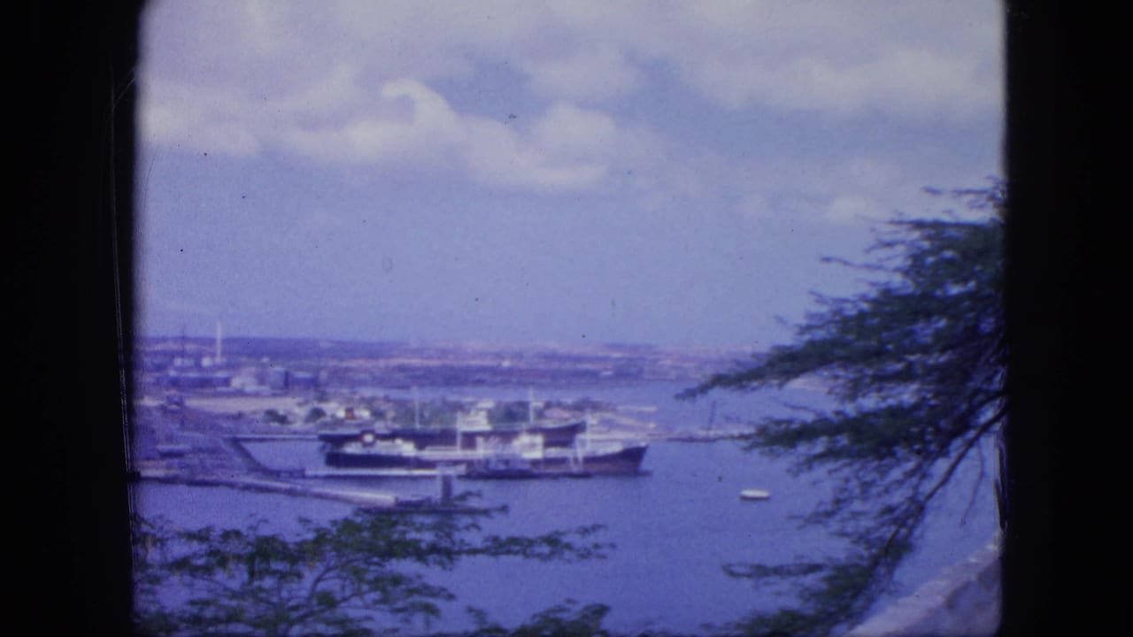 Elevated 1964 Nassau harbor frame with a moored ship, small boats, distant port area, clouds, and trees along the edge.
