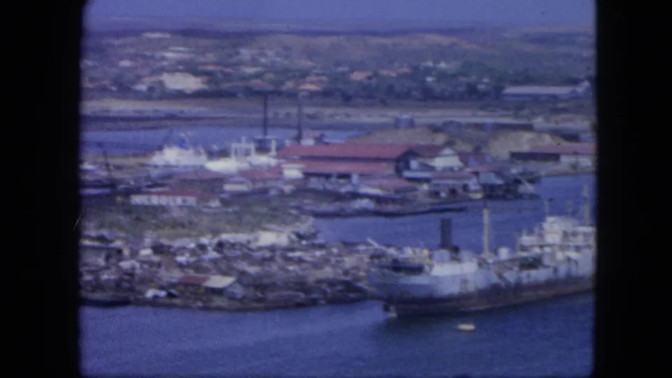 Nassau harbor in 1964 with docked vessels, waterfront buildings, storage tanks, shoreline, and soft 8mm color.