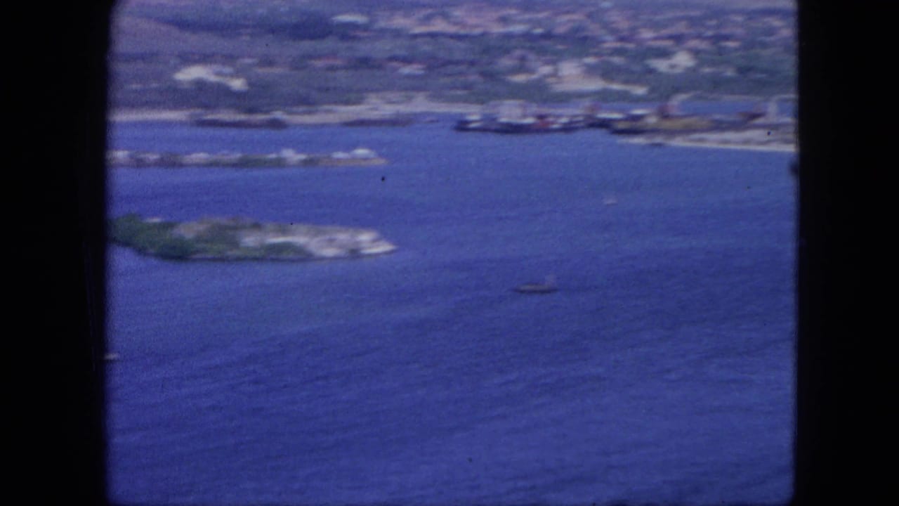 Aerial harbor view with blue water, shoreline development, small boats, and low green islands.