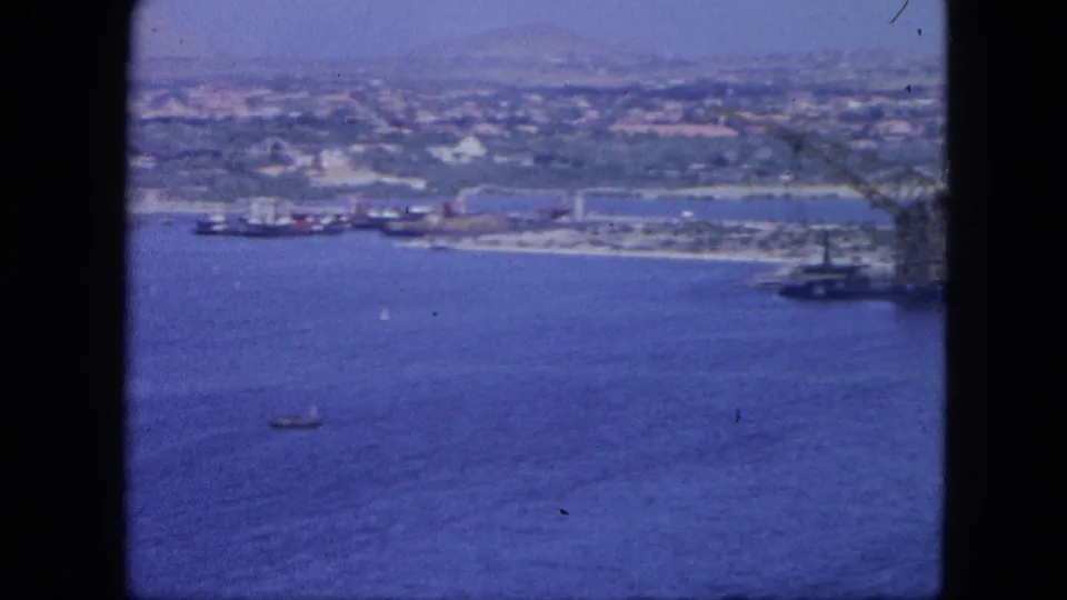 1964 Nassau harbor aerial showing cargo ships along the shore, dock areas, blue water, and a small boat in the foreground.