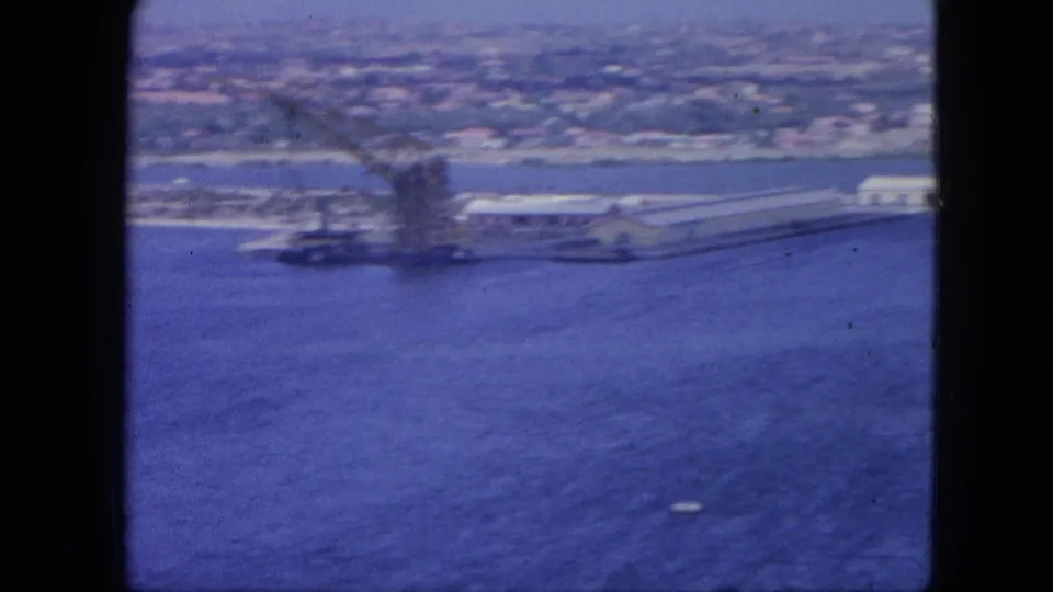 Nassau harbor aerial view from 1964 with a prominent dockside crane, waterfront buildings, blue water, and a small boat.