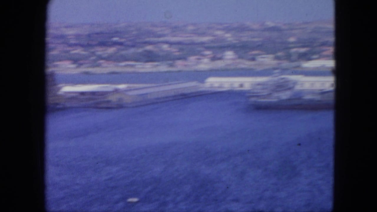 1964 Nassau harbor seen from above, with blue bay water, white waterfront buildings, and a soft distant shoreline.