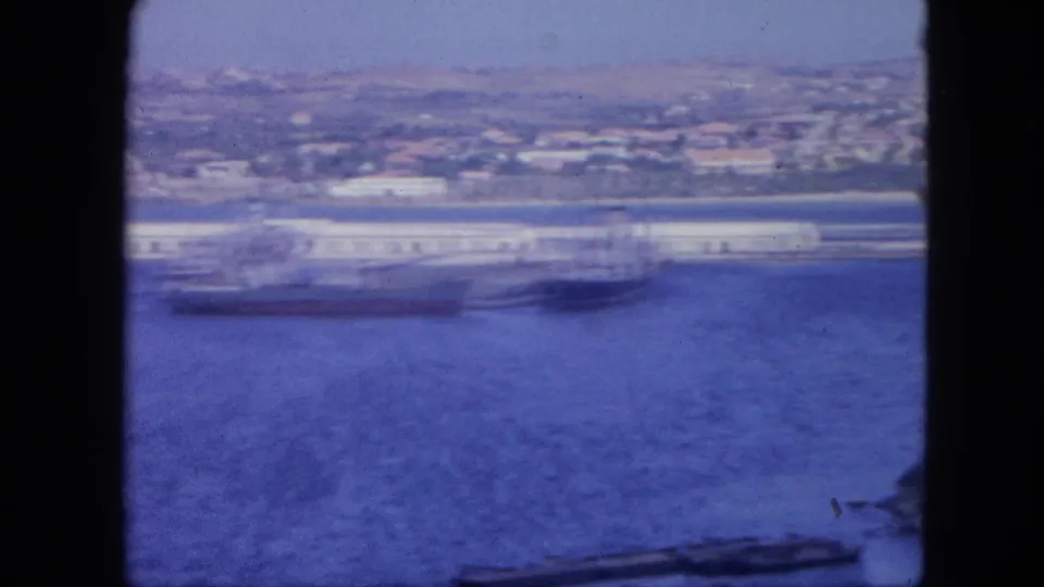 1964 Nassau waterfront with a large vessel at the dock, blue bay water, and hillside buildings in the distance.