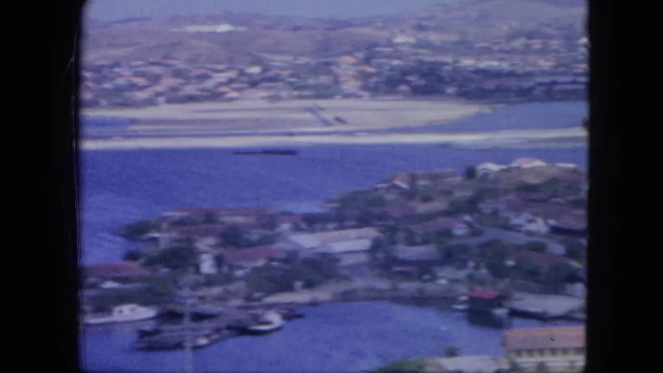 1964 Nassau harbor from an elevated angle, showing small boats, waterfront buildings, docks, and shoreline development.