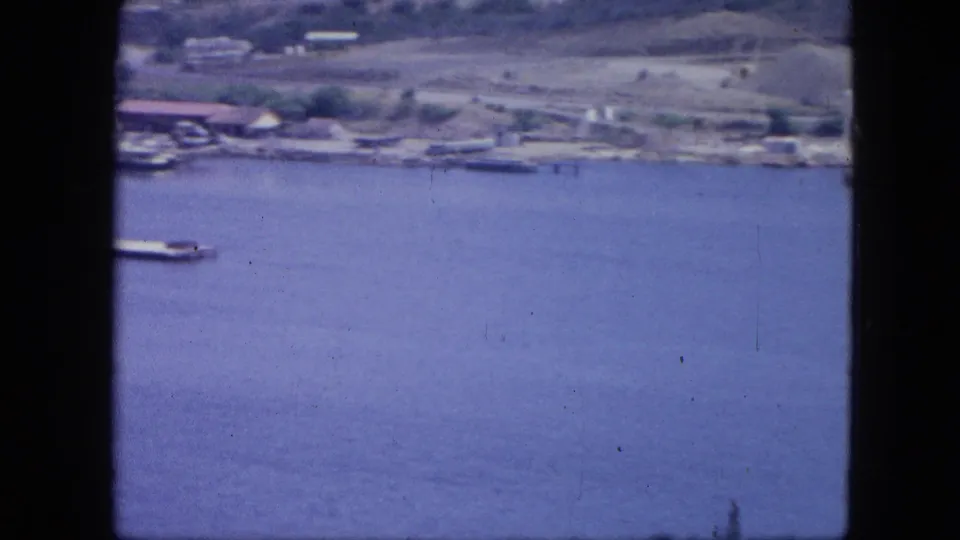 Nassau aerial frame showing open harbor water, a partial pier or vessel, shoreline development, and hills in the distance.