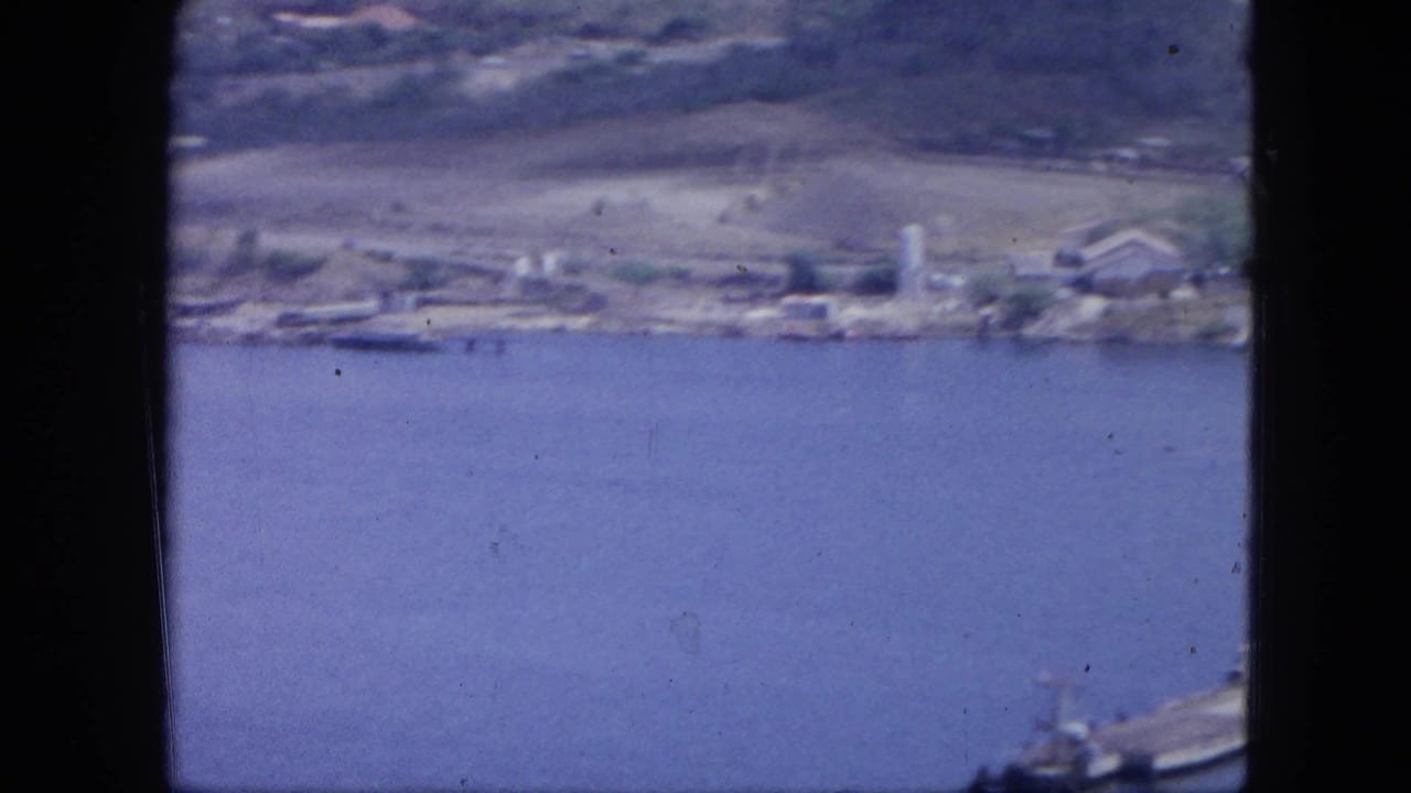 Elevated view across blue harbor water toward shoreline buildings and hills.