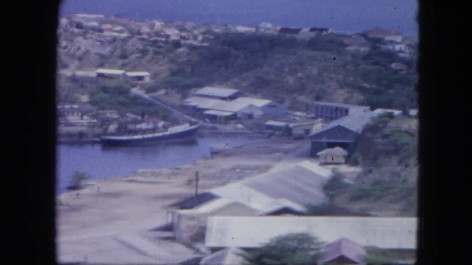 1964 Nassau frame showing rooftops, roads, harbor edge, and clustered waterfront buildings from above.