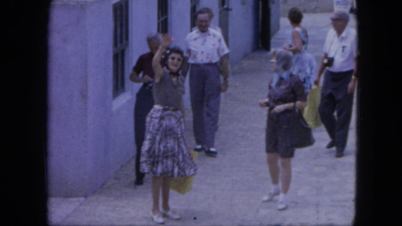 In Nassau, Bahamas in 1964, tourists in summer clothing walk through an alley as a woman with a yellow bag waves up at the camera.